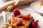 Slices of baked oatmeal on a plate with a spoon, sliced berries, and chocolate chips.