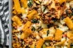Baked bolognese ziti with zucchini, tomatoes, mushrooms, and melted mozzarella cheese in a dish with a wooden spoon.