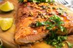 Baked cilantro lime salmon on a wooden board with fresh cilantro, garlic, lime juice, and honey on top.