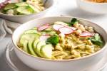 Mexican pozole verde with shredded chicken and hominy in two bowls with jaalpeno, cilantro, and radishes.