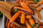 Roasted baby carrots with olive oil, honey, salt, and pepper served on a baking sheet with a wooden spoon and parsley.