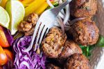 Vegetarian lentil meatballs served in a bowl with bell peppers, red cabbage, tomatoes, and greens served with a fork.