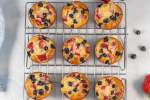 Muffins made with pancake batter with strawberries and blueberries on a wire rack.