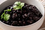 Cooked black beans with onion, garlic, and spices in a white bowl served on a brown napkin. 