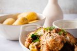 Crockpot rotisserie chicken served in a white dish with slow cooker potatoes on the side.