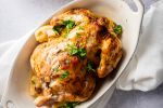 Rotisserie chicken with potatoes served in a white dish with lemon, garlic, and parsley.