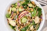 Apple and spinach salad with red onions, cucumbers, and goat cheese in a bowl with walnuts and balsamic dressing on the side.