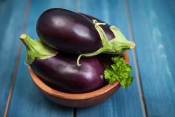 Two eggplants in a wooden dish on a blue counter.