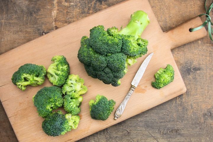 Broccoli on a cutting board with florets and a knife.