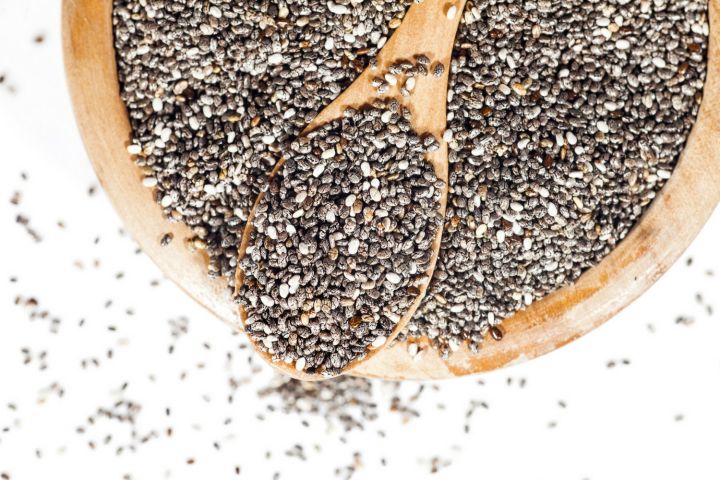 Loose chia seeds in a bowl with a wooden spoon.