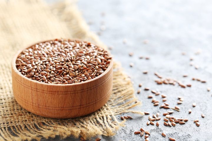 A bowl of flaxseeds on a burlap napkin with some loose flax seeds.