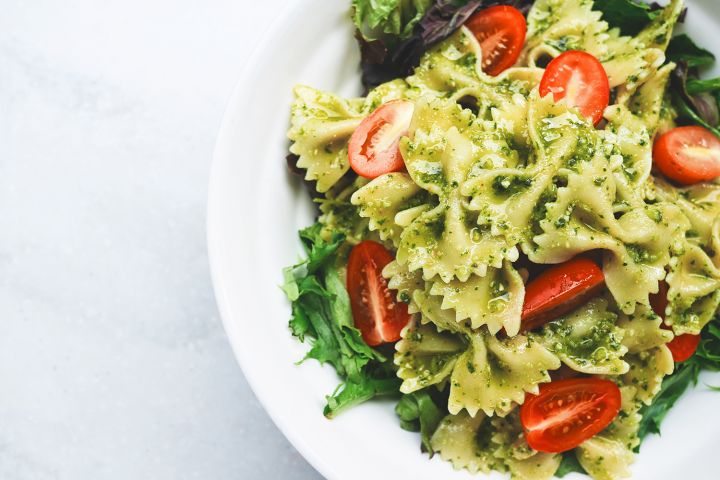 Vegan pasta with cherry tomatoes, spinach pesto, and fresh spinach leaves.