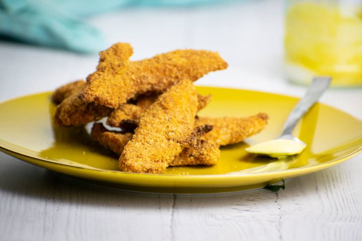 Almond chicken tenders piled on a plate with honey mustard.