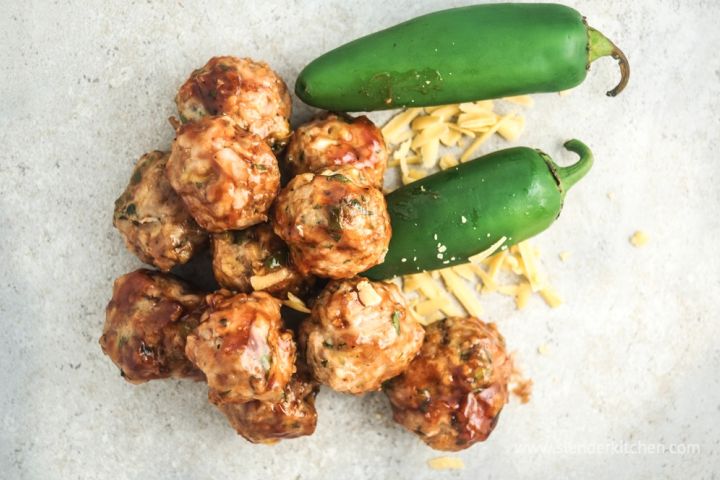 Barbecue cheddar meatballs on a cutting board with fresh jalapenos on the side.