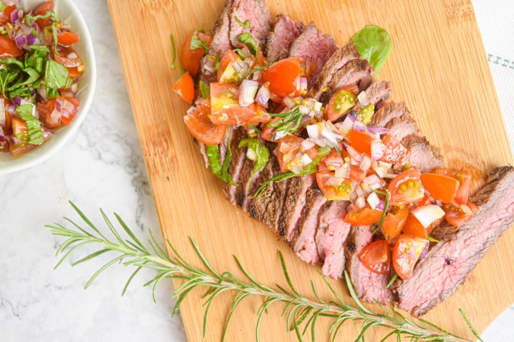 Flank steak with tomato basil salad on a cutting board with rosemary.