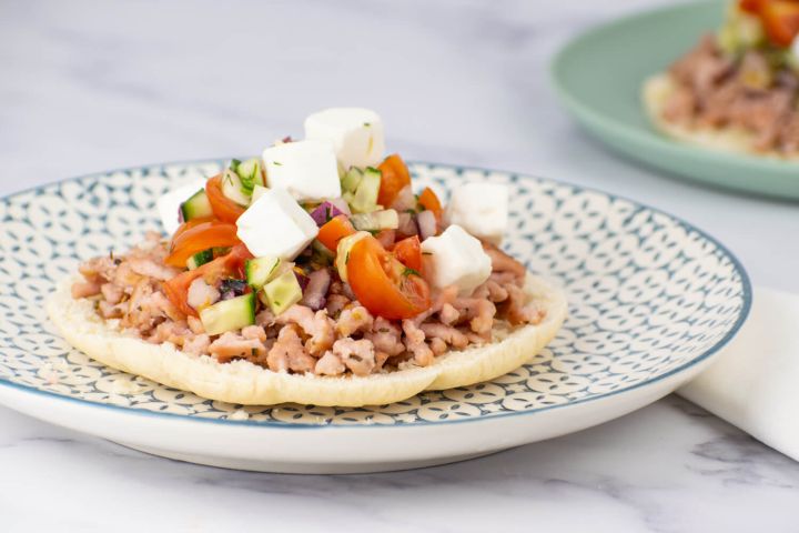 Greek turkey tostadas with tomatoes, cucumbers, and feta cheese on toasted pita bread.