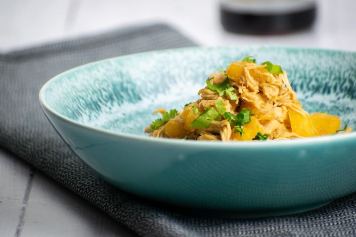Slow cooker Hawaiian chicken with pineapple and cilantro in a blue bowl.