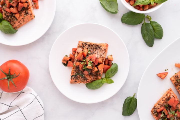 Italian salmon with a tomato basil salsa on a plate with fresh basil on the side.