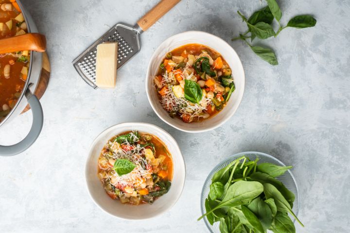 Italian bean and vegetable soup with cannellini beans, tomatoes, carrots, spinach, and zucchini in two bowls with Parmesan cheese.