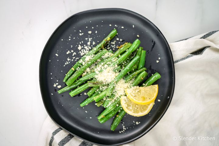 Parmesan green beans with lemon and garlic on a black plate.