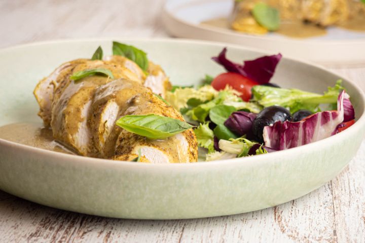Slow cooker coconut basil chicken on a plate with creamy sauce and salad on the side.