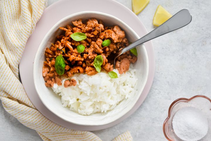Thai basil ground turkey in a bowl with white rice and Thai basil leaves. 