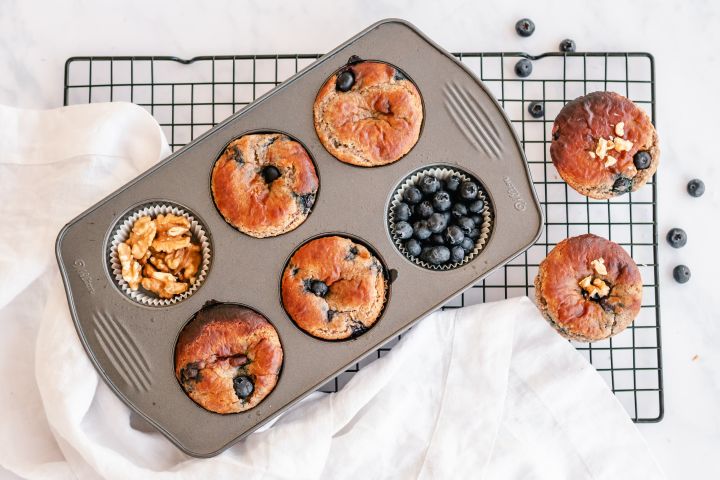 Almond flour yogurt blueberry muffins in a muffin tray with extra blueberries and walnuts on the side.