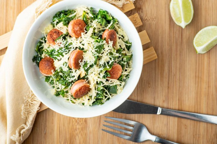Angel hair pasta with sausage and kale in a bowl with a fork and knife.