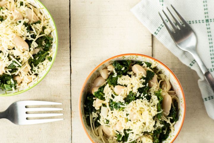 Pasta with white beans and kale in a bowl with lemon wedges.