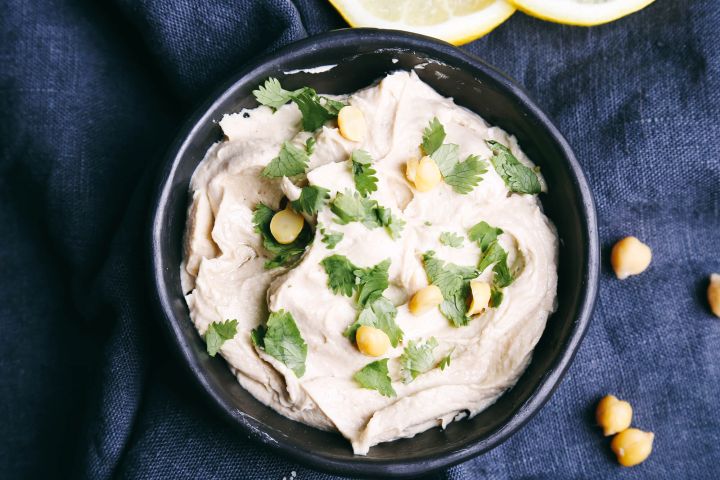 Artichoke hummus with lemon and chickpeas in a bowl with a blue napkin.