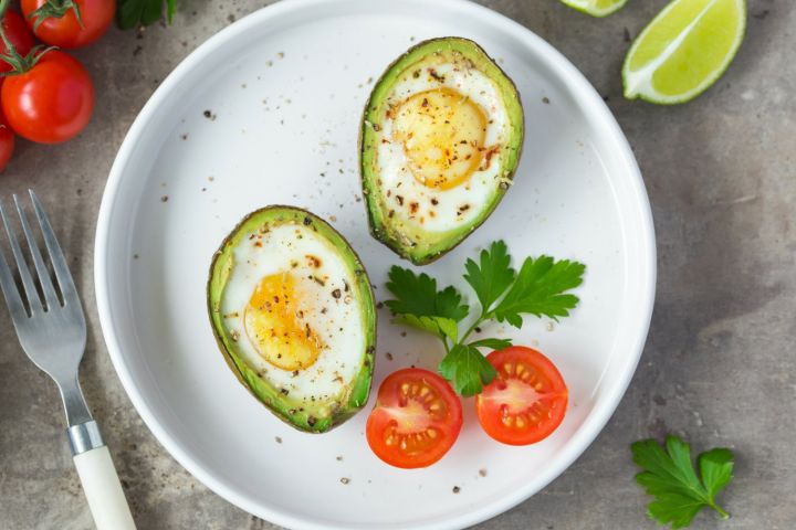 Two avocado baked eggs on a cutting board with salt and pepper.