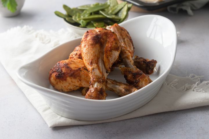 Baked chicken drumsticks with a paprika spice rub served in a white dish with vegetables on the side.