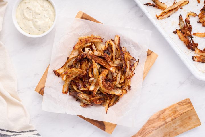 Baked onion straws with a crispy Parmesan coating on parchment paper with dipping sauce on the side. 