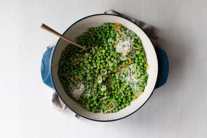 Sauteed peas with garlic, shallots, lemon, and shredded Parmesan cheese in a ceramic dish.