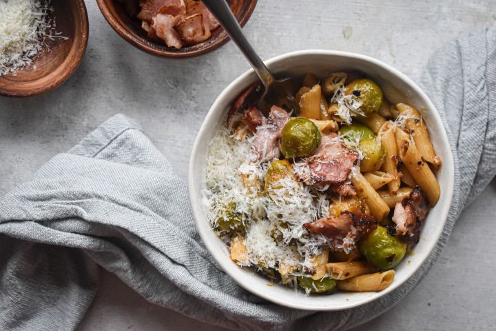 Brussels sprout pasta with bacon and Parmesan cheese in a bowl with a spoon.