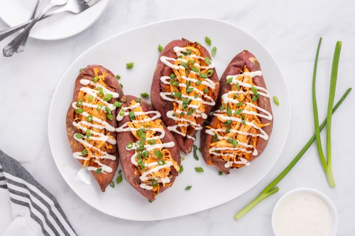 Buffalo chicken stuffed sweet potatoes on a plate with ranch dressing and green onions.