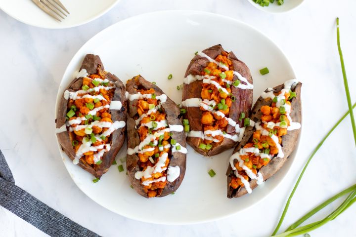 Buffalo chickpea stuffed sweet potatoes on a plate drizzled with ranch dressing and green onions.