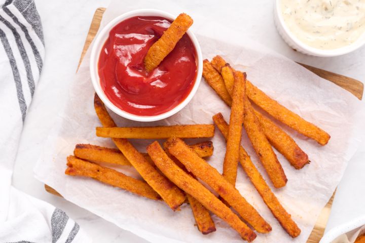 Butternut squash fries baked until crispy and served on parchment paper with ketchup and herb sauce.
