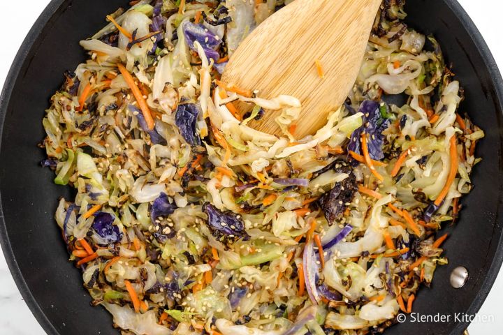 Cabbage stir fry in a black skillet with sliced green cabbage, carrots, and soy sauce.