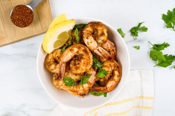 Cajun shrimp coated in seasoning in a bowl with parsley and lemon.