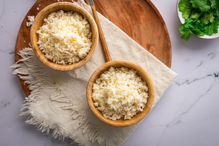 Cauliflower rice made with fresh cauliflower florets in two wooden bowls with fresh herbs on the side.