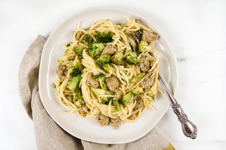 Chicken sausage pasta with broccoli on a plate with parmesan cheese and a fork.