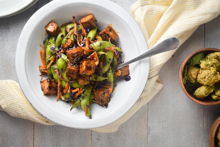 Chili Glazed Tofu with cabbage, snap peas, carrots, and tofu in a bowl with a napkin.