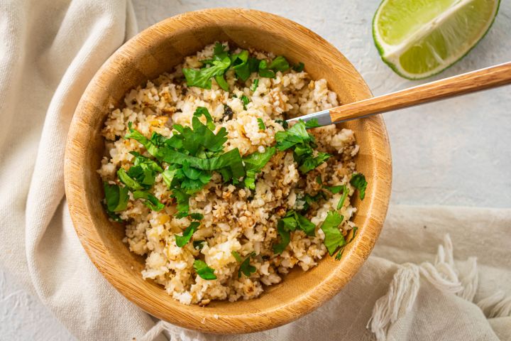 Cilantro lime cauliflower rice with fresh cilantro leaves and lime wedges in a wooden bowl.