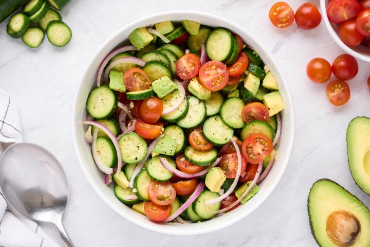 Cucumber salad with tomatoes, avocado, red onion, and vinaigrette in a large bowl.