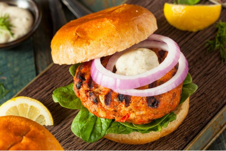 Curry salmon burgers with yogurt sauce on a bun with red onion and herbs.