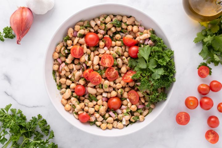 Easy bean salad with chickpeas, white beans, shallots, cherry tomatoes, and fresh herbs in a bowl.