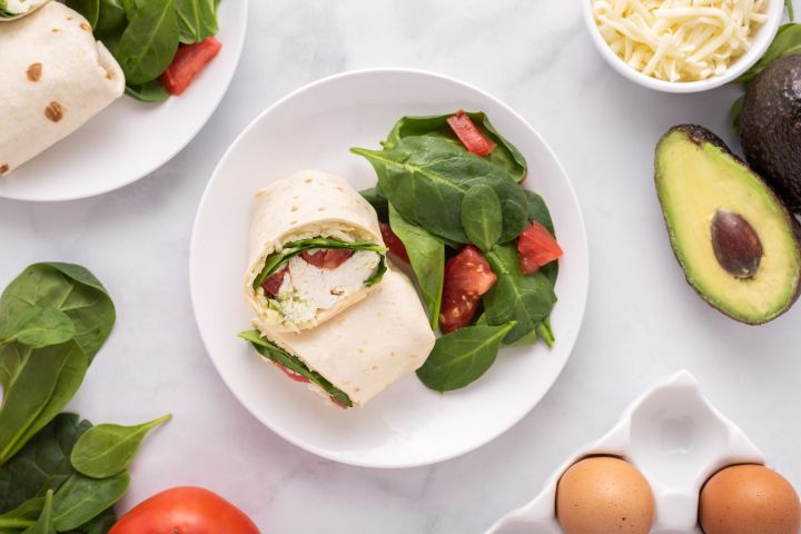 Egg white breakfast sandwich with cooked egg whites, avocado, tomatoes, spinach, and mozzarella wrapped in a tortilla.