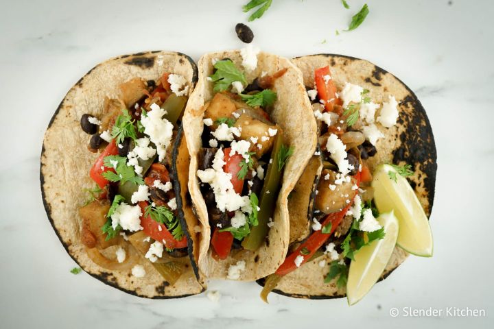 Baked eggplant fajitas with peppers and onions in corn tortillas with queso fresco.