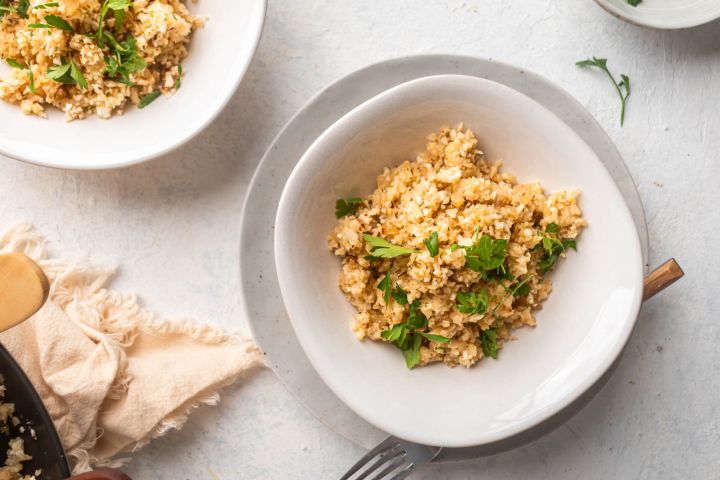 Garlic parmesan cauliflower rice with fresh parsley in a bowl with a wooden fork. 